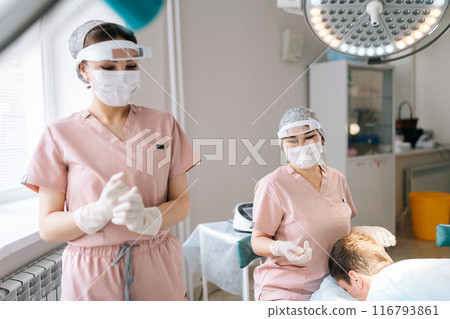 Dermatologist in mask performing local anesthesia to back of head in recipient area prior to hair transplant surgery. Male patient receiving hair loss treatment injections in scalp by trichologist. 116793861