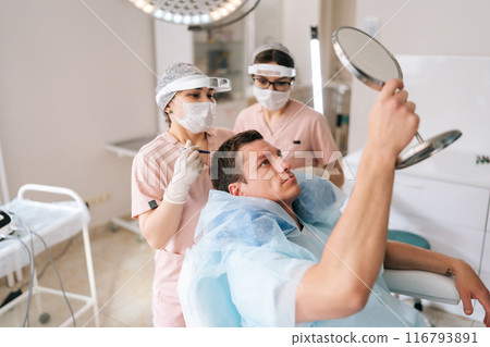 Top view shot of male patient with hair loss problem talking with female trichologist marking who with pencil new hairline on head before hair transplantation surgery. Concept of baldness treatment Top view shot of male patient with hair loss problem talking with female trichologist marking who with pencil new hairline on head before hair transplantation surgery. Concept of baldness treatment 116793891