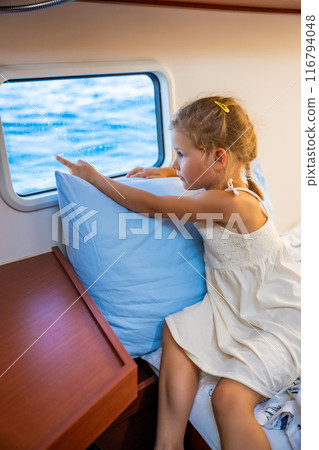 Blond little girl sits in the cabin of a yacht and looks out the window during a sea crossing. Yacht life concept Blond little girl sits in the cabin of a yacht and looks out the window during a sea crossing. Yacht life concept 116794048