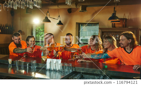 Group of soccer fans cheerfully talking together, laughing while clinking glasses of beers in moment of celebration win of favorite team. Group of soccer fans cheerfully talking together, laughing while clinking glasses of beers in moment of celebration win of favorite team. 116794121