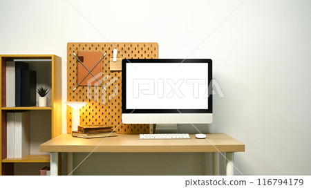 Blank screen computer desktop on wooden table next to wooden bookshelf, Home office 116794179