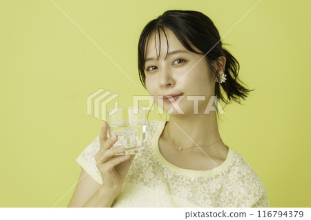 黃色背景下拿著一杯水的年輕女子的肖像 黃色背景下拿著一杯水的年輕女子的肖像 116794379