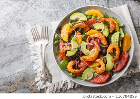 Shrimp salad with citrus fruits such as orange and grapefruit, as well as avocado, red onion and leafy greens close-up in a plate. Horizontal top view 116794859