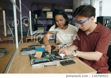 Colleagues Repairing Laptop Together In Workshop 116794922