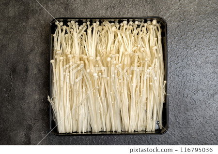 A tray of white mushrooms is on a dark surface 116795036