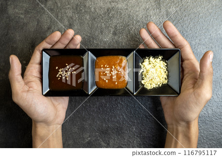 A person is holding three small black plates with different sauces 116795117