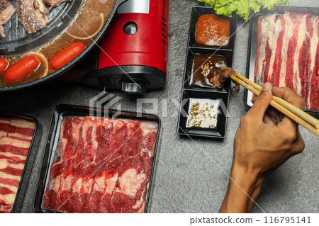 A couple is eating meat with chopsticks and dipping sauces A couple is eating meat with chopsticks and dipping sauces 116795141