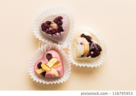 chocolate sweets in the form of a heart with fruits and nuts on a colored background. top view with space for text, holiday concept chocolate sweets in the form of a heart with fruits and nuts on a colored background. top view with space for text, holiday concept 116795953