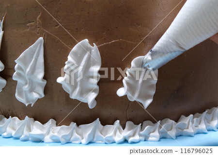 A woman pastry chef with a pastry bag in her hands squeezes cream on a cake in a home kitchen. Professional chef at work on bakery kitchen. culinary, baking and cooking food concept, home cooking A woman pastry chef with a pastry bag in her hands squeezes cream on a cake in a home kitchen. Professional chef at work on bakery kitchen. culinary, baking and cooking food concept, home cooking 116796025