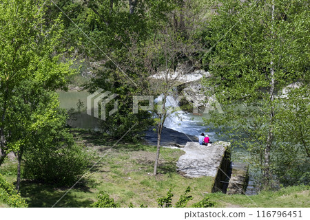two people sitting on a rock at the edge of a stream 116796451