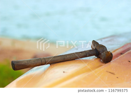 Old rusty hammer rests on the plastic hull of the boat in the background of the water 116799375