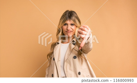Dissatisfied stylish transgender woman in trench coat showing thumbs down Dissatisfied stylish transgender woman in trench coat showing thumbs down 116800993
