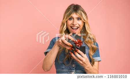 Happy transgender woman offering small gift box against pink background 116801010