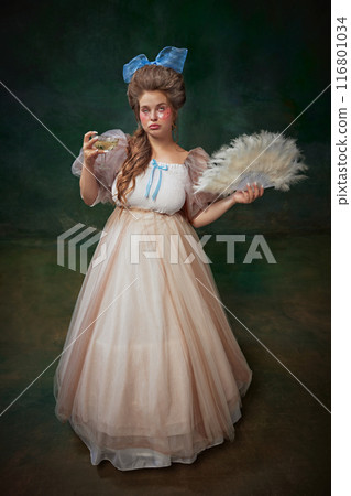 After party. Portrait of elegant young women with under eye patches, standing with feather fan and drinking champagne against vintage green background 116801034