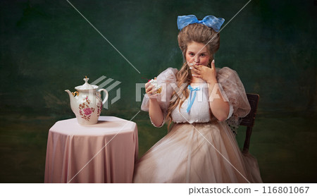 Portrait of medieval princess in elegant dress sitting at table and eating delicious cake against dark vintage background. 116801067