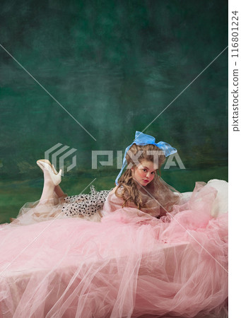 Medieval royal person, woman in tulle gown with blue bow resting on pink fabric against vintage green background. Art gallery 116801224
