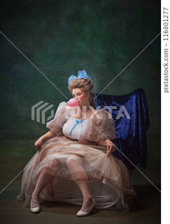 Beautiful woman in period attire, royal person sitting on chair with pink bubble gum against vintage green background 116801277