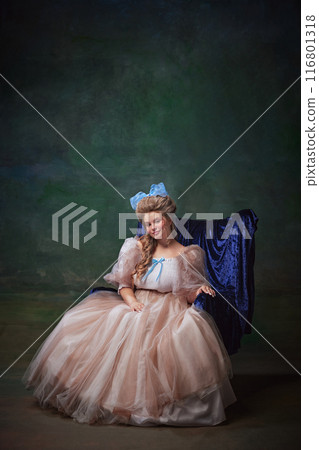 Portrait of elegant young woman in luxurious period dress sitting on bleu chair against vintage green background. medieval royal person 116801318