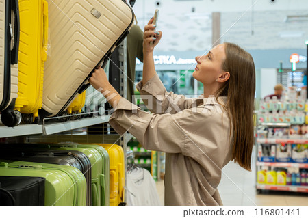 A woman is shopping for a suitcase in a retail store. She reaches out to select a suitcase from a shelf and scans the barcode on it using her smartphone. A woman is shopping for a suitcase in a retail store. She reaches out to select a suitcase from a shelf and scans the barcode on it using her smartphone. 116801441