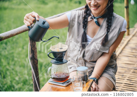 Tourist woman pouring hot water onto ground coffee beans with paper filter to make a drip coffee. Tourist woman pouring hot water onto ground coffee beans with paper filter to make a drip coffee. 116802805