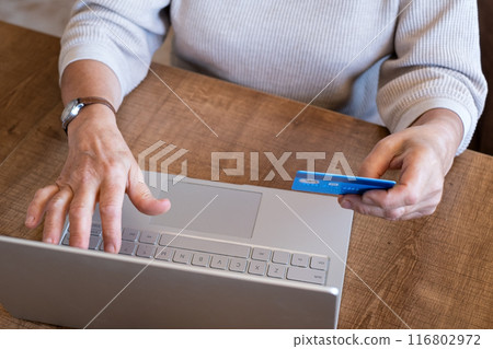 A woman is making an online purchase or payment, utilizing card and a laptop  116802972