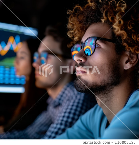 Team of professional stock traders working late night analyzing graphs on multiple computer screens 116803153