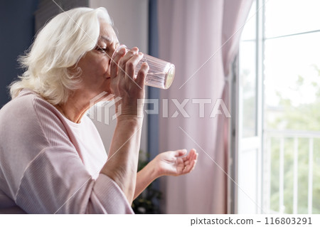 Senior woman takes pill with glass of water in hand. Senior woman takes pill with glass of water in hand. 116803291