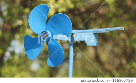 A blue vane weathervane spins in the wind in the summer. A blue vane weathervane spins in the wind in the summer. 116803729
