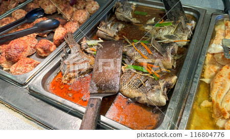 a buffet display featuring cooked whole fish in a flavorful sauce, meatballs, and filleted fish, ready to be served a buffet display featuring cooked whole fish in a flavorful sauce, meatballs, and filleted fish, ready to be served 116804776