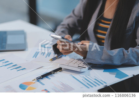 Attractive and cheerful millennial Asian businesswoman receiving a good message or email through her smartphone, sitting at her desk. Attractive and cheerful millennial Asian businesswoman receiving a good message or email through her smartphone, sitting at her desk. 116806136