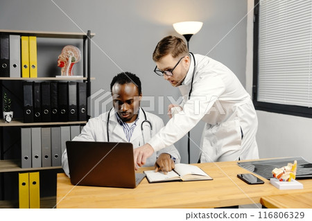 Doctor discussing diagnosis with young colleague in office 116806329