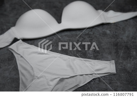 The bra and panties are white on a grey background, the panties are in focus from below, the bra is out of focus from above. Underwear, clothes. High quality photo 116807791