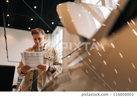 Thoughtful male customer holding papers, checking vehicle characteristics during choosing car in modern dealership center. Concept of choosing and buying new auto at showroom. 116808001