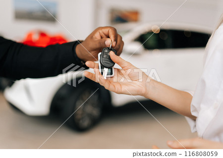 Closeup side view of unrecognizable female buyer getting car key and congratulation from black auto dealer male buying new auto in dealership. Woman car owner during handing over keys at showroom. 116808059