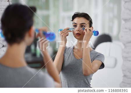 A young woman is doing a relaxing face massage using cold cryo spheres. 116808391