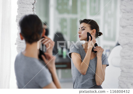 Facial skin care. A woman is doing a face massage using gouache stones. Facial skin care. A woman is doing a face massage using gouache stones. 116808432