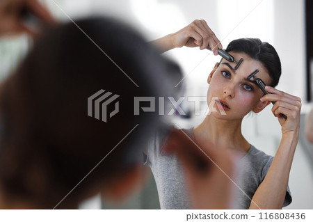 A young woman massages her face with gouache while looking in the mirror. 116808436