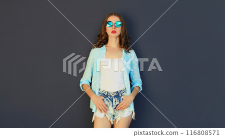 Stylish modern young woman in glasses, shorts posing on black wall background 116808571