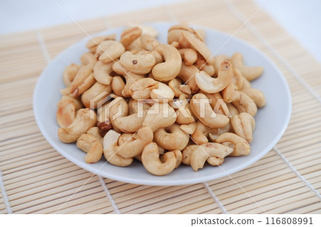 Roasted cashew nuts in white bowl on bamboo mat, stock photo 116808991