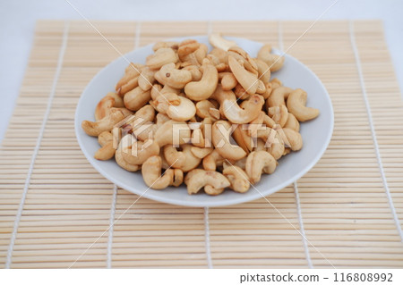 Roasted cashew nuts in white bowl on bamboo mat, stock photo Roasted cashew nuts in white bowl on bamboo mat, stock photo 116808992