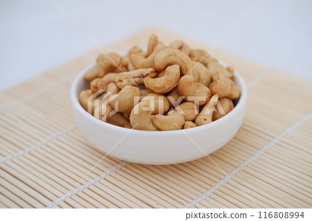 Roasted cashew nuts in white bowl on bamboo mat, stock photo Roasted cashew nuts in white bowl on bamboo mat, stock photo 116808994