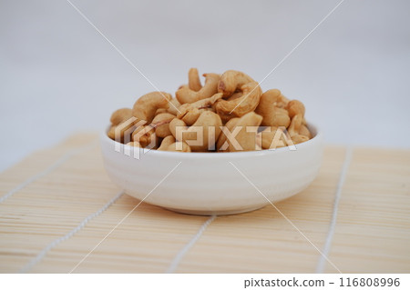 Roasted cashew nuts in white bowl on bamboo mat, stock photo 116808996