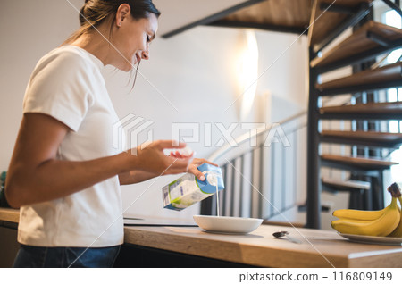 Young woman pouring milk while preparing breakfast Young woman pouring milk while preparing breakfast 116809149