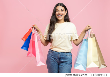 Excited woman wearing casual T-shirt and jeans holding shopping bags visiting fashionable boutique 116809311