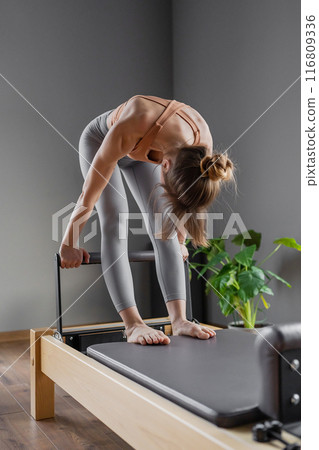 Woman doing Pilates exercise for core and back muscles on Reformer machine with determination and focus on strength body 116809336