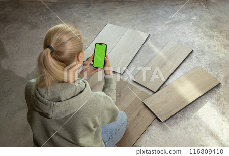 Interior designer Holds Smartphone with Green Chroma Key Screen above Luxury Vinyl Wood Samples On Concrete Floor In House. Choosing, Selecting Waterproof Flooring. Home Reconstruction. Horizontal. Interior designer Holds Smartphone with Green Chroma Key Screen above Luxury Vinyl Wood Samples On Concrete Floor In House. Choosing, Selecting Waterproof Flooring. Home Reconstruction. Horizontal. 116809410