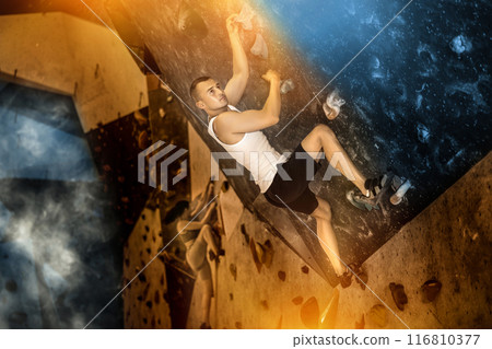 Young man climbing on artificial rock wall in rock-climbing gym Young man climbing on artificial rock wall in rock-climbing gym 116810377
