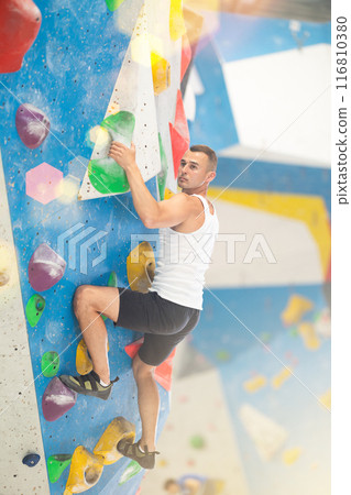 Young man climbing on artificial rock wall in rock-climbing gym 116810380