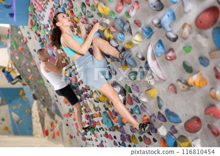 Middle-aged woman climbing on artificial rock wall in rock-climbing gym 116810454