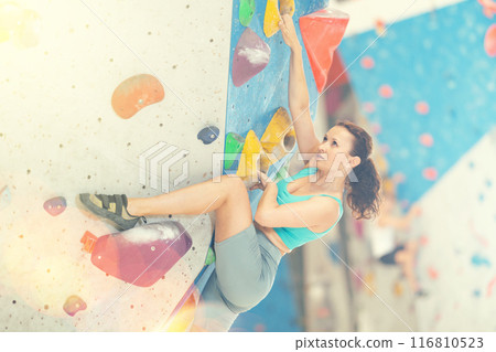 Middle-aged woman climbing on artificial rock wall in rock-climbing gym Middle-aged woman climbing on artificial rock wall in rock-climbing gym 116810523